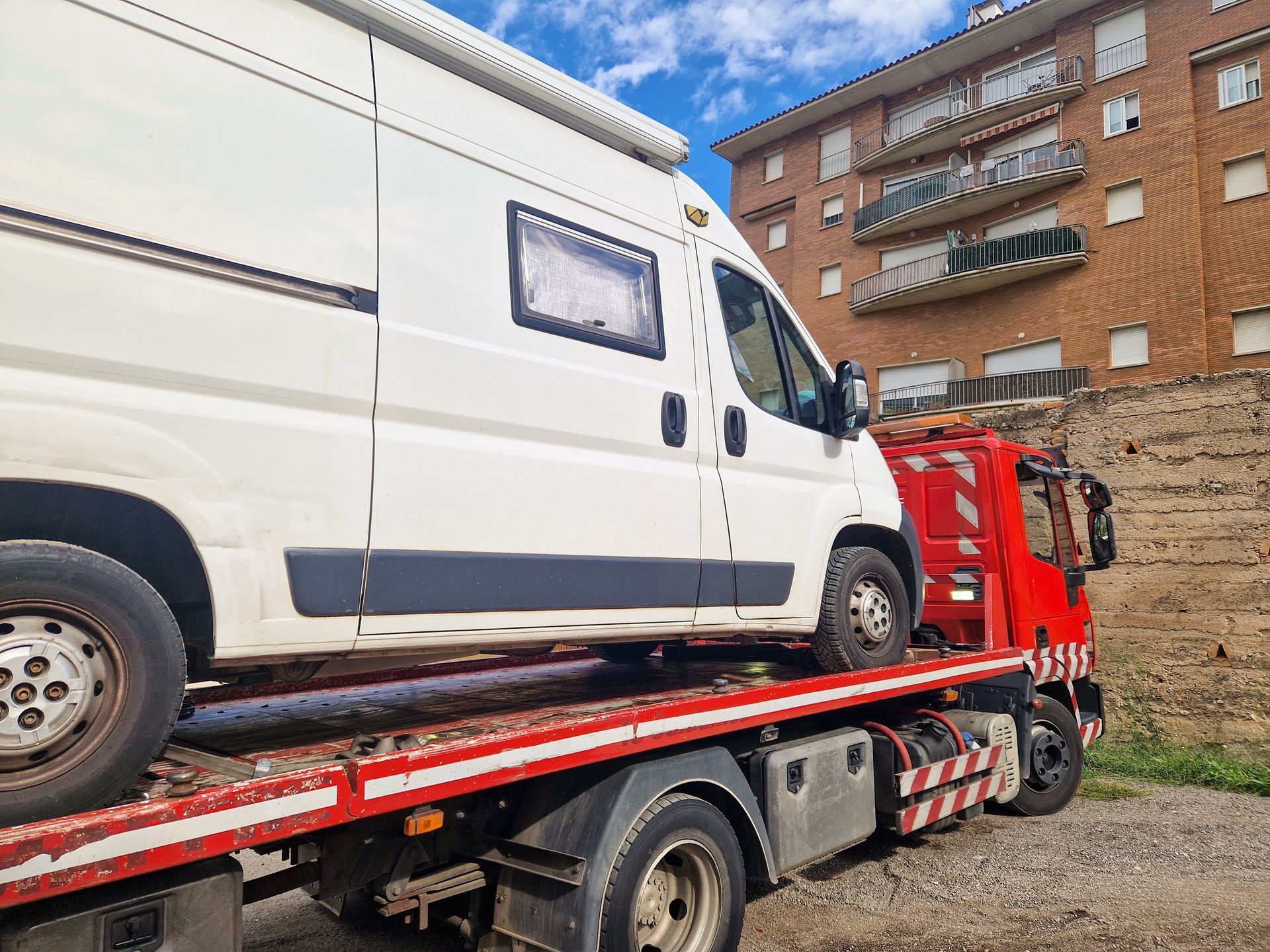 White cargo van secured on a red tow truck flatbed outside a brick building.