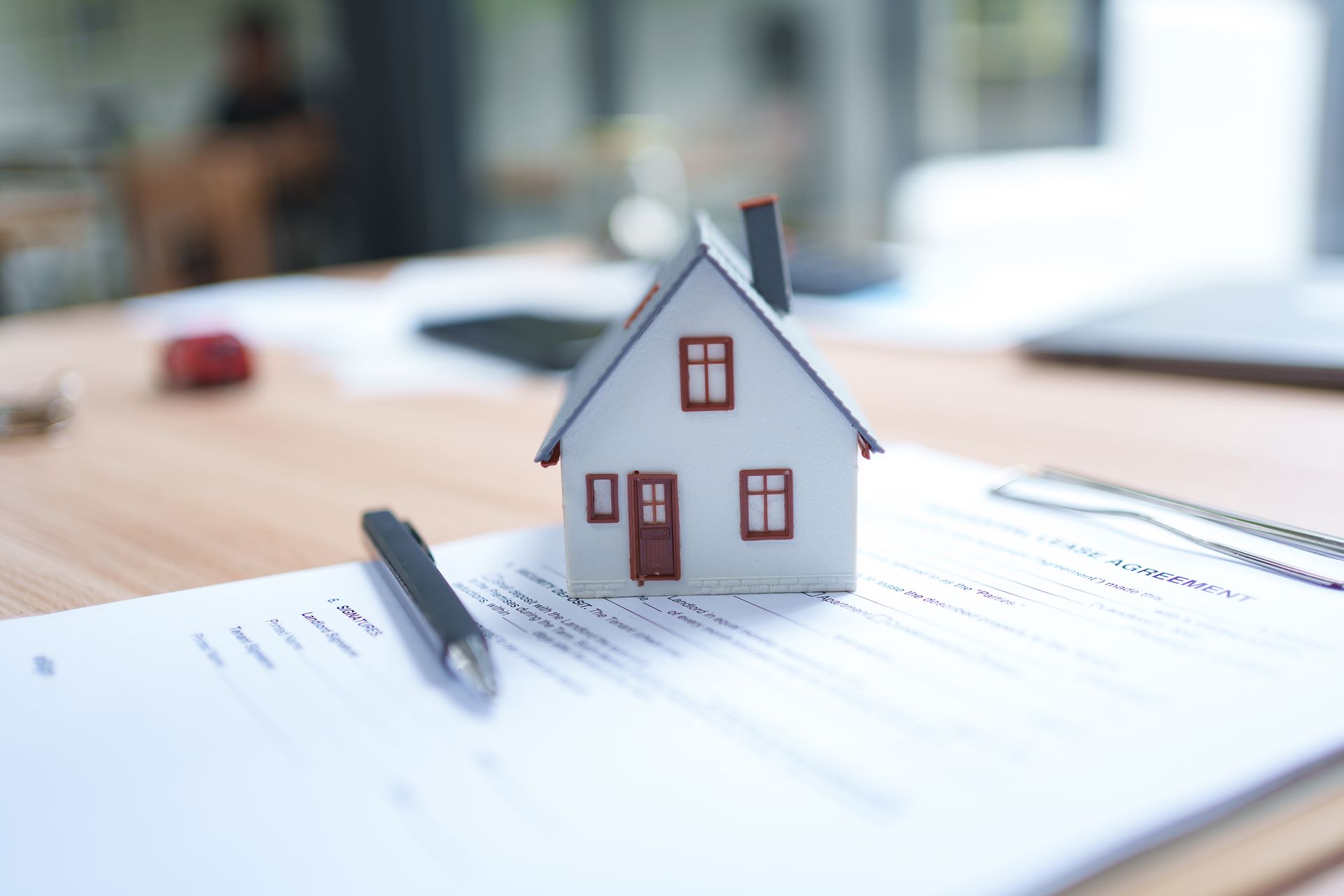 Toy house and pen on paperwork on a desk, suggesting a home loan or real estate planning.