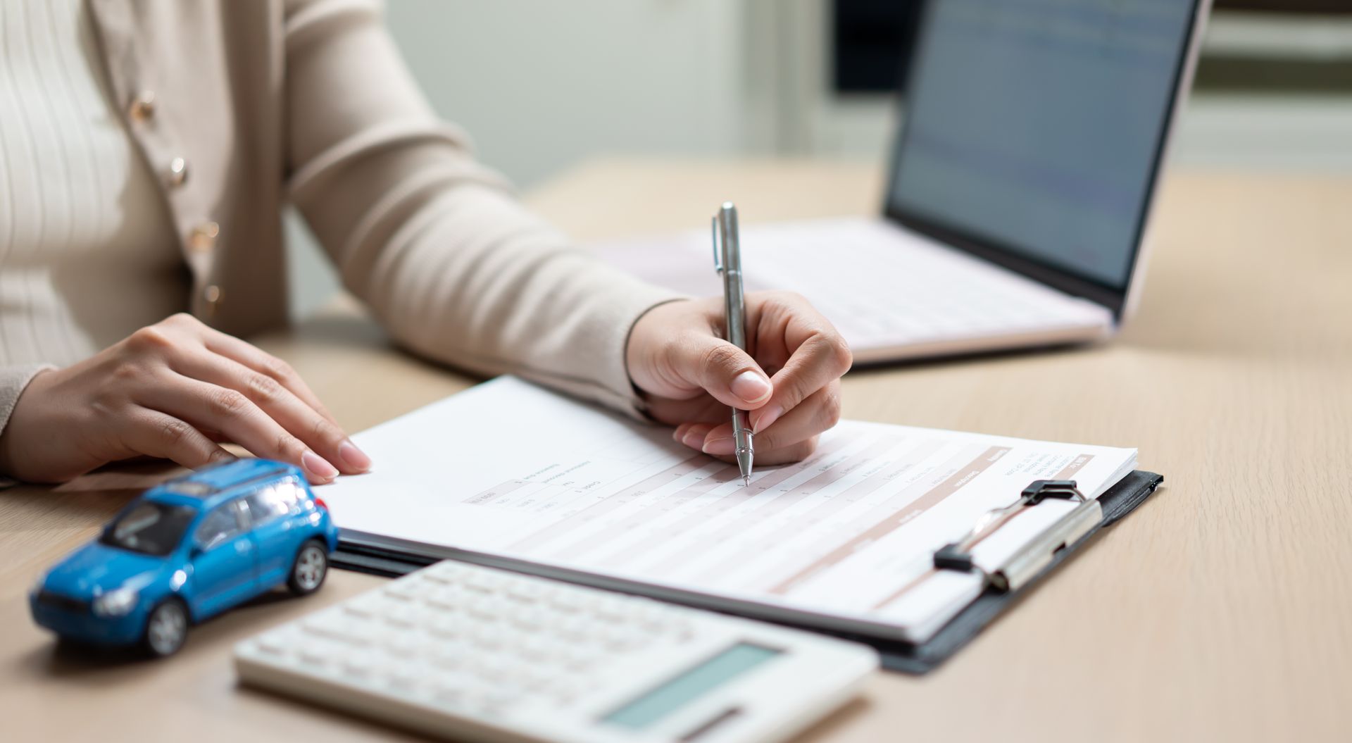 Person filling out paperwork at a desk with a calculator and a blue toy car
