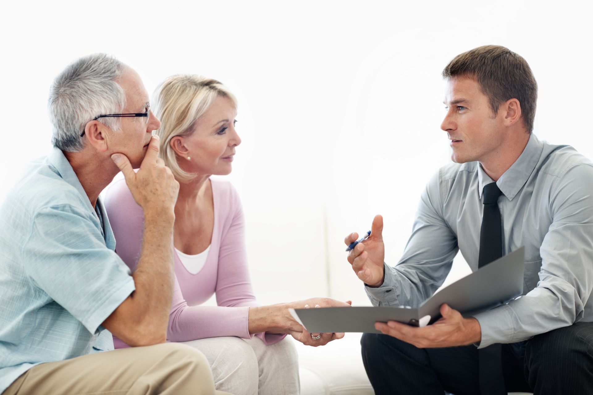 Three people in a meeting, one man speaking while two listen and hold a laptop.