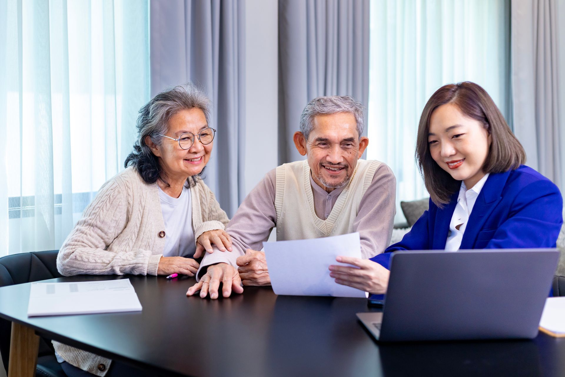 Three people reviewing documents at a conference table with a laptop in a bright office