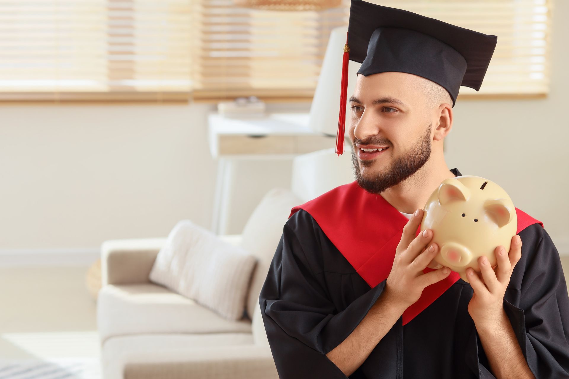 Graduation portrait of a smiling graduate in cap and gown holding a piggy bank