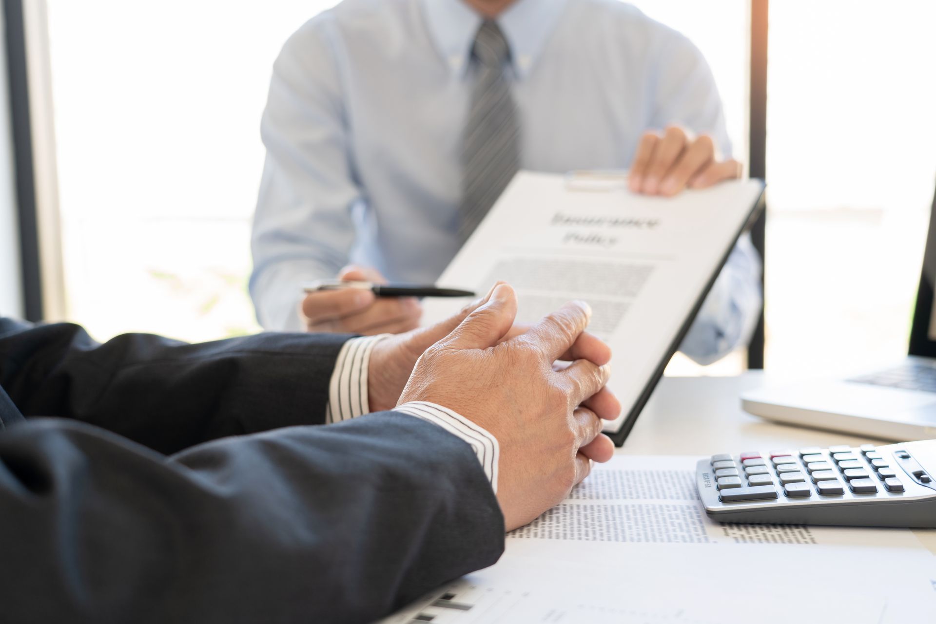 Business meeting with a person signing a document across from a calculator on a desk