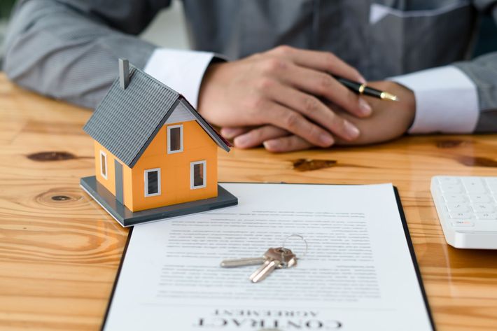 Small house model and keys on a real estate contract with a person’s hands in the background