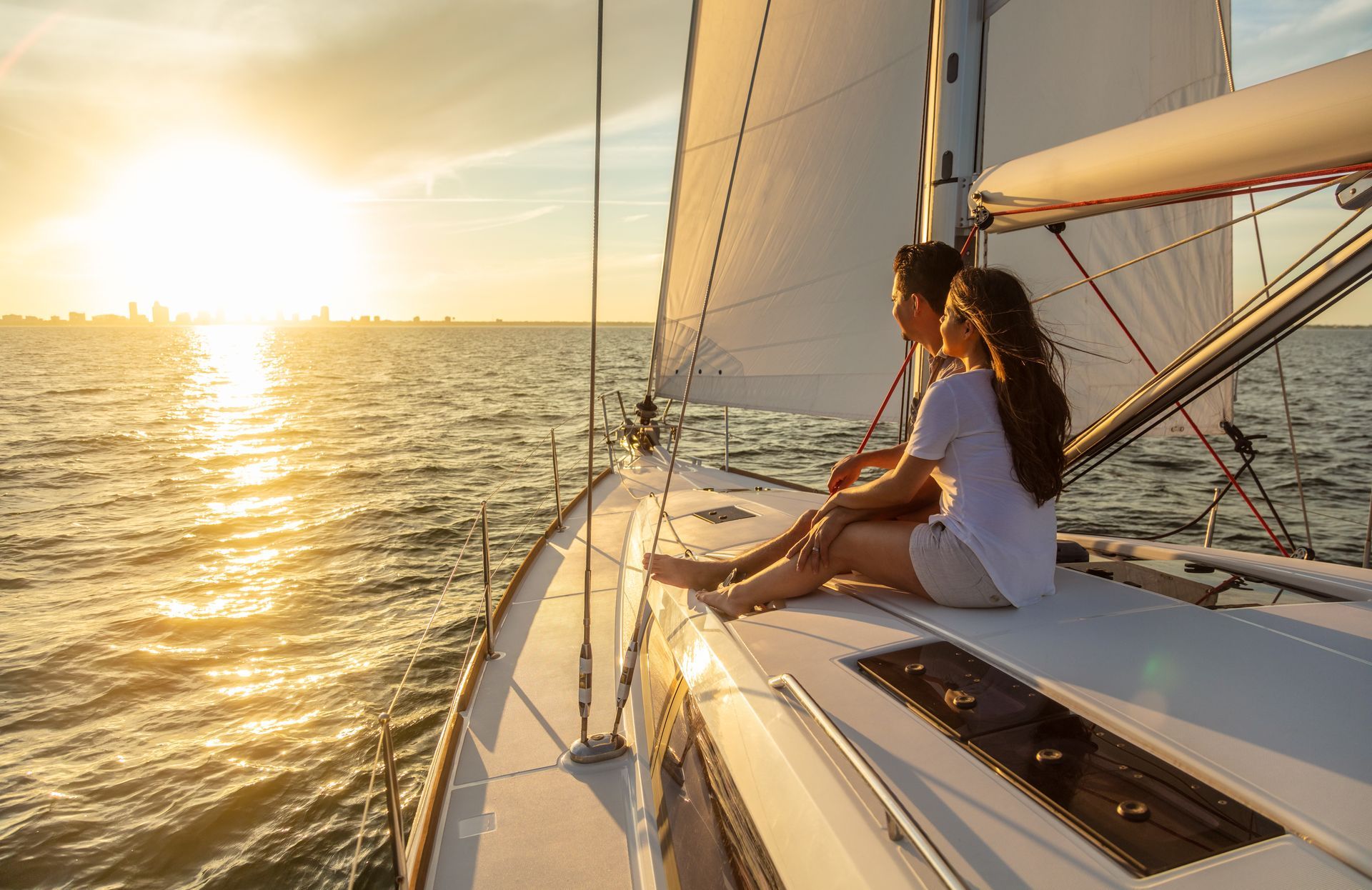 Person sitting on a sailboat deck at sunset, looking toward the glowing sea