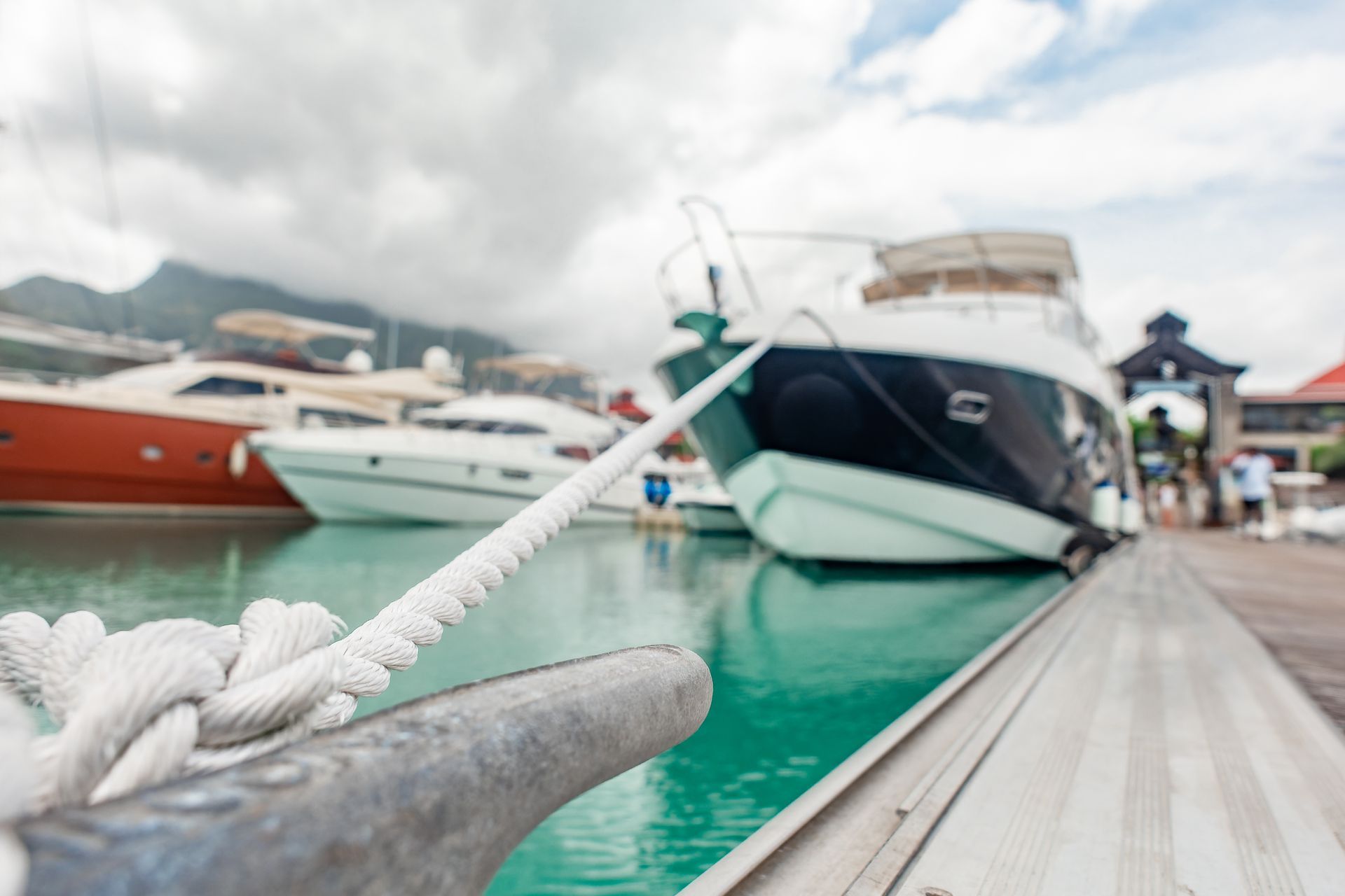 Luxury boats docked beside a wooden pier on turquoise water under cloudy skies