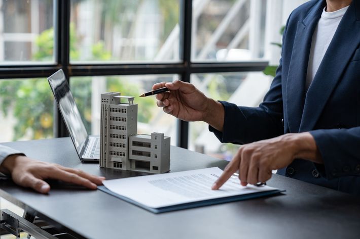 Business meeting at a desk with architectural model, laptop, and people discussing plans