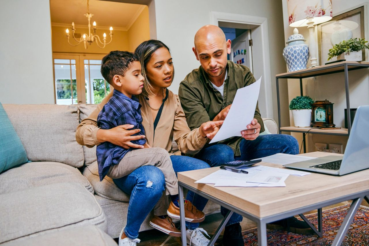 Family reviewing documents together on a couch beside a laptop in a bright living room