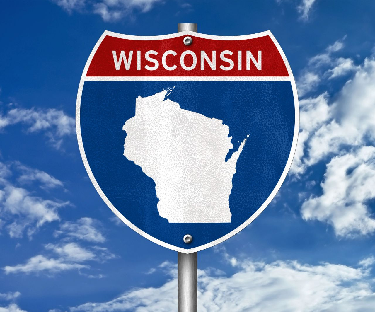 Wisconsin state highway shield sign with white state silhouette on blue and red background against a cloudy sky