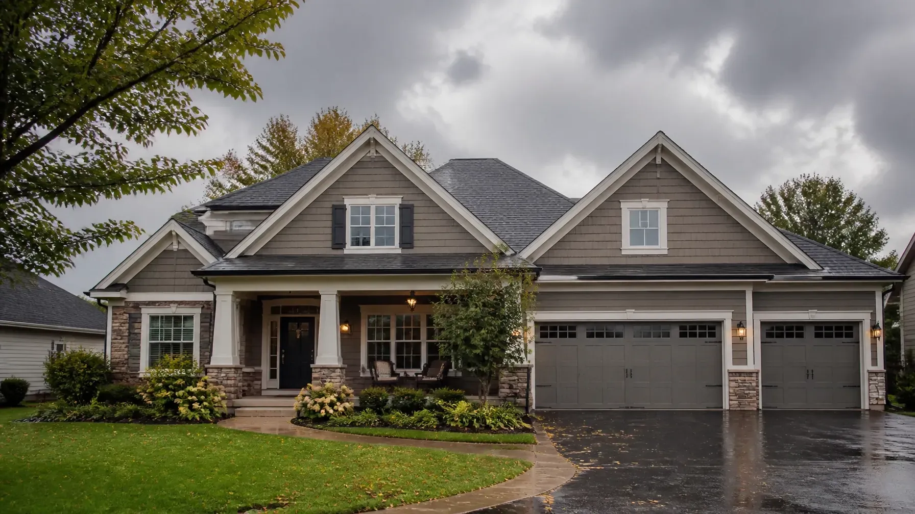 Suburban house with gray siding, front porch, and double garage on a rainy day