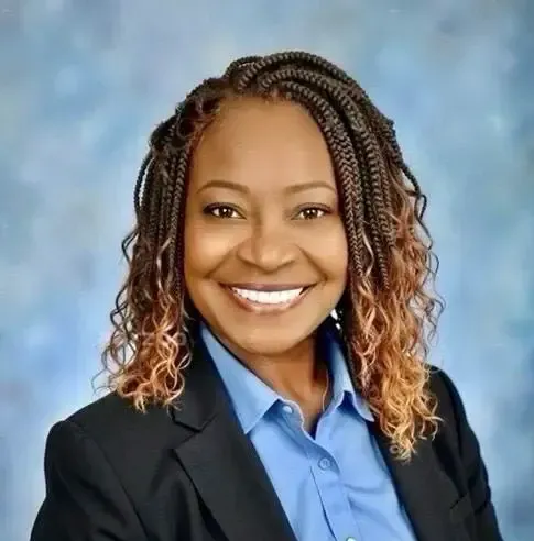 Smiling professional portrait of a woman in a black blazer and blue shirt against a blue background