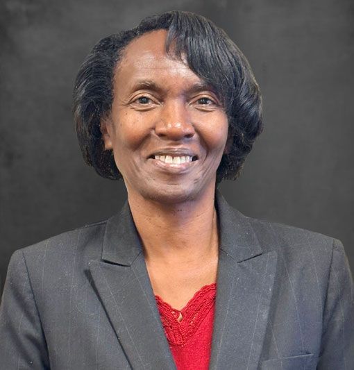 Portrait of a smiling person in a dark blazer and red top against a gray background