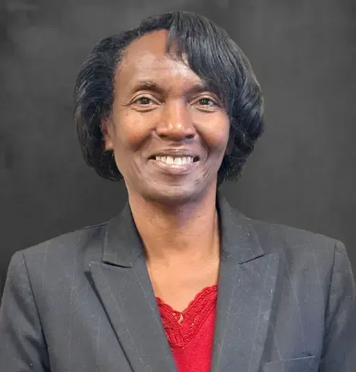 Smiling person in a black blazer and red top against a dark gray background