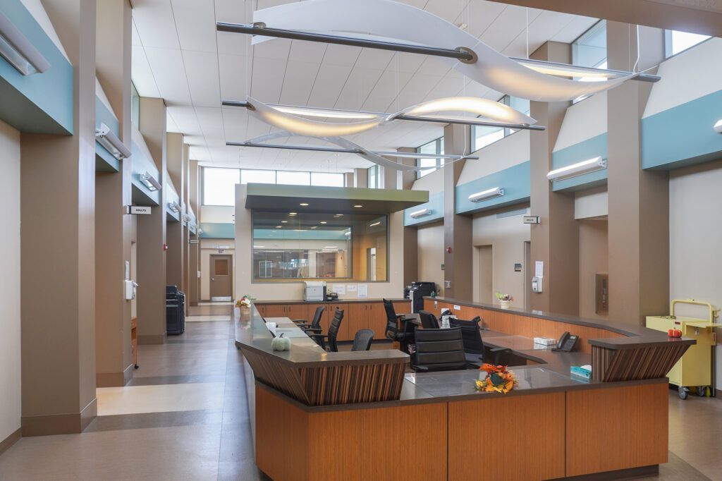 Bright hospital lobby with a central reception desk and skylit ceiling.