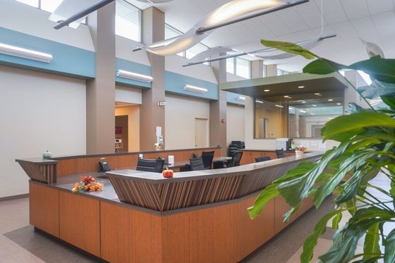 Modern office reception desk with wood paneling, computers, and a bright open lobby with plants