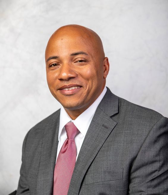 Portrait of a smiling man in a gray suit and pink tie against a light gray background