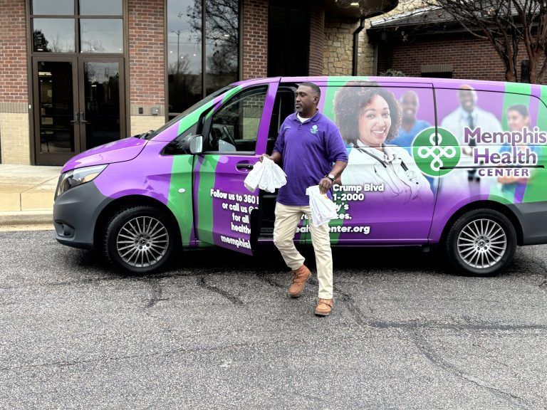 Man standing beside a purple Memorial Health van with healthcare graphics outside a building