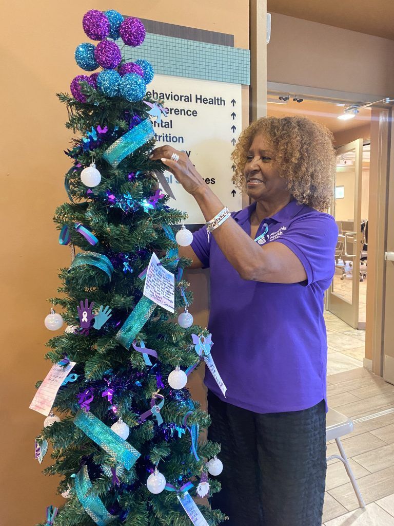 Woman decorating a purple-and-blue Christmas tree in a mall corridor