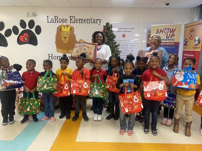 Children holding decorated bags pose in a school hallway at LaRose Elementary, with staff behind them.