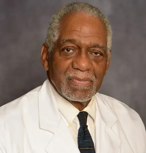 Portrait of a man in a white coat and dark tie against a gray studio background