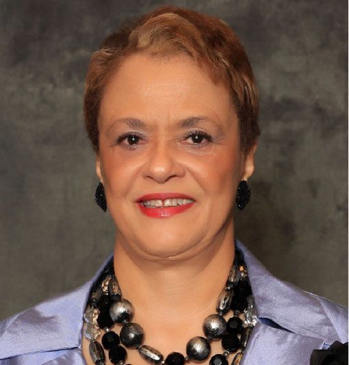 Studio portrait of a smiling person in a light blue blazer and black beaded necklace