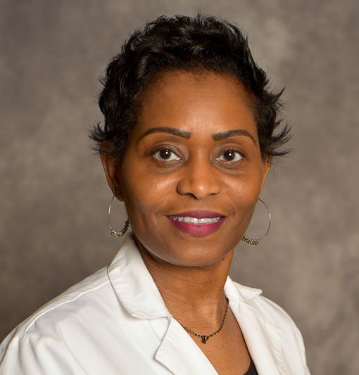 Portrait of a smiling woman in a white blazer against a neutral studio background