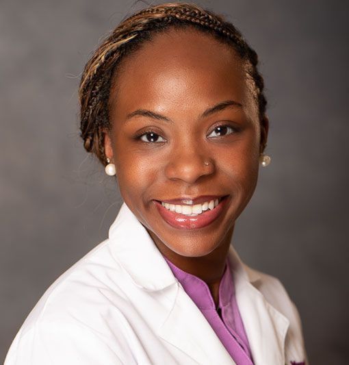 Smiling person in a white coat against a gray studio backdrop