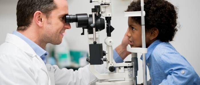 Doctor examining a child with an eye chart through a slit-lamp microscope in a clinic