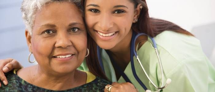 Smiling nurse with stethoscope beside a patient in a hospital setting