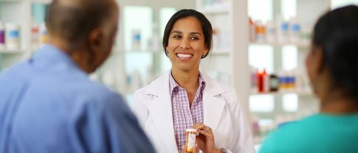 Smiling pharmacist in white coat talking with two customers in a bright pharmacy