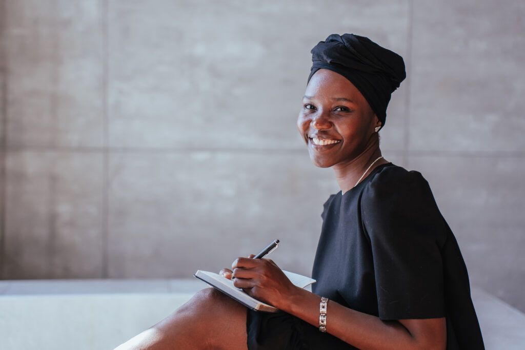 Smiling person seated with a notebook and pen in a bright room
