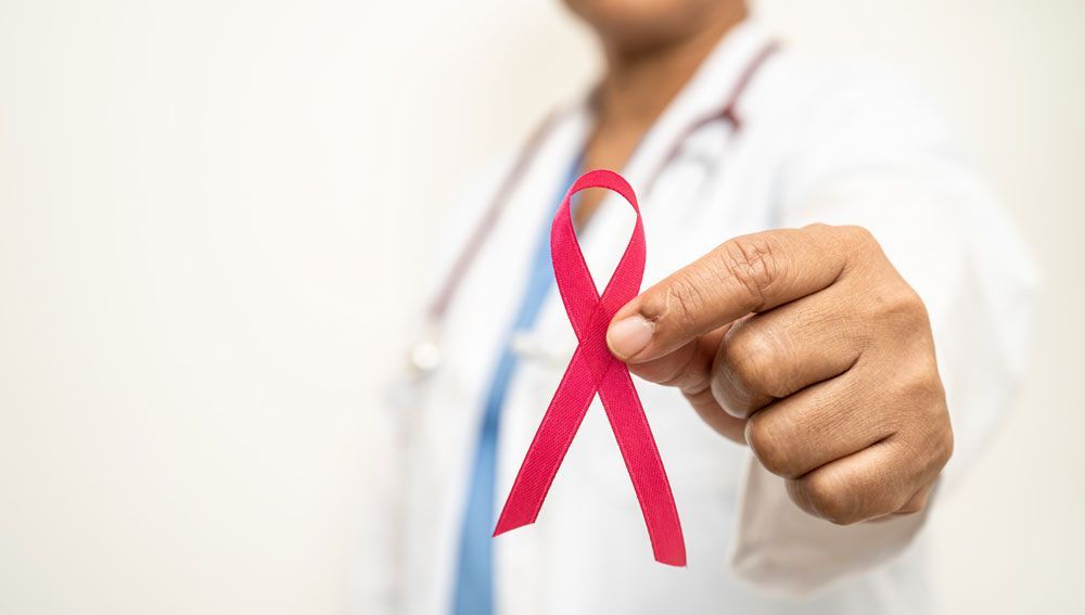 Doctor holding a pink breast cancer awareness ribbon in a clinic