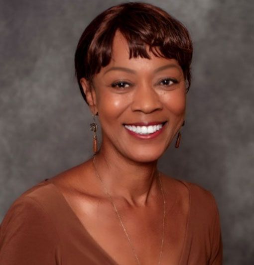 Smiling woman with short brown hair in a brown top against a gray backdrop