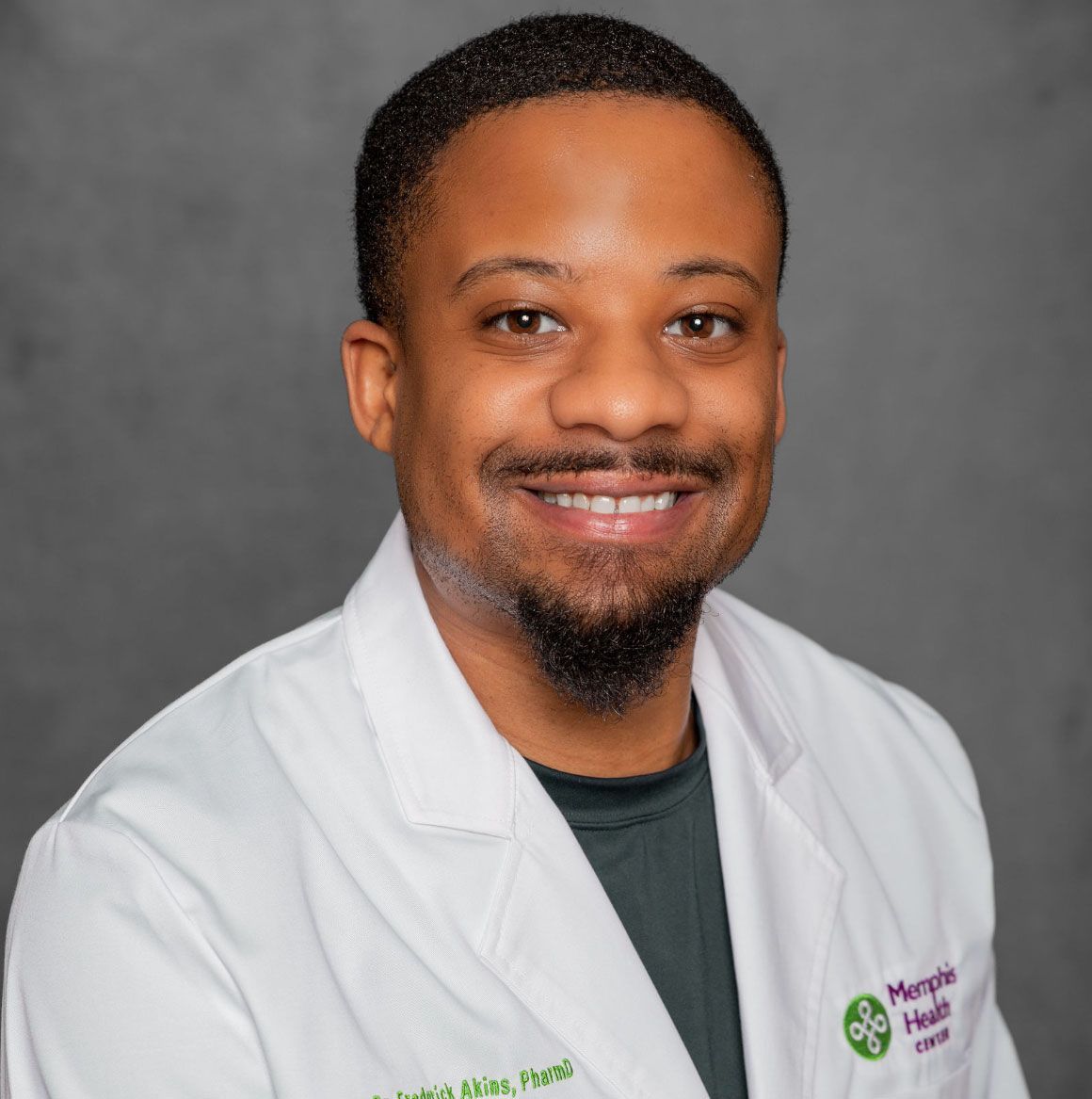 Portrait of a smiling healthcare professional in a white coat against a gray studio backdrop