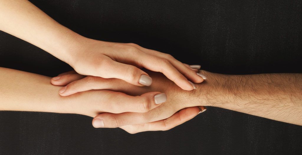 Two hands clasped together in a supportive gesture against a dark background