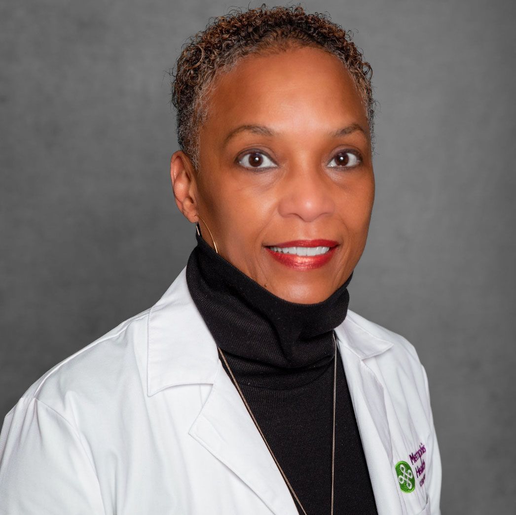 Portrait of a woman in a white coat and black turtleneck, smiling against a gray background