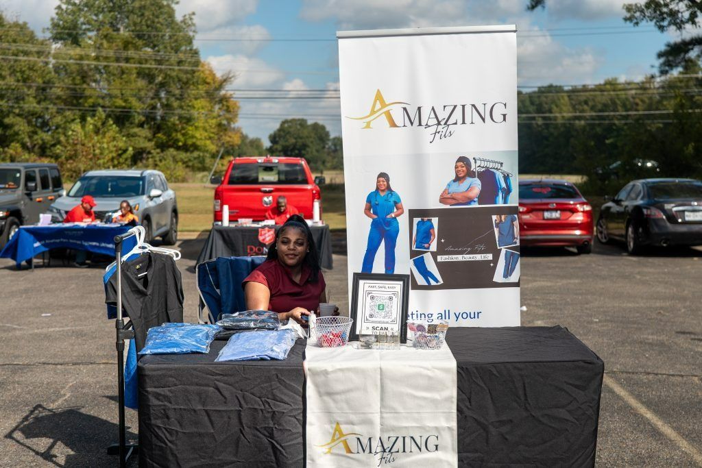 Vendor booth with banners and a table of shirts at an outdoor parking lot event