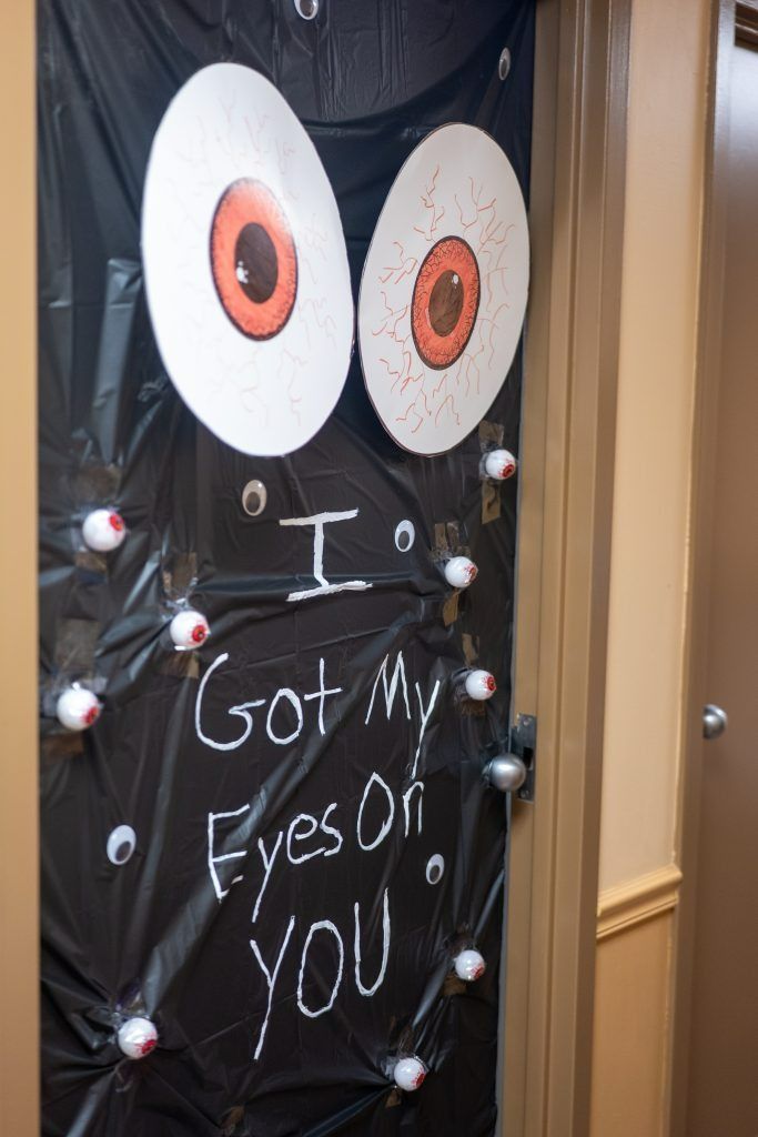 Spooky black Halloween sign with big orange eyes and white chalk text reading “I Got My Eyes on YOU”