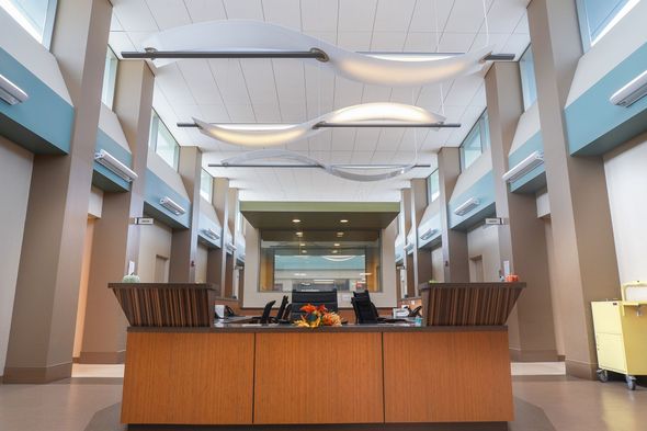 Empty modern lobby with a central wooden reception desk and hanging white ceiling lights.