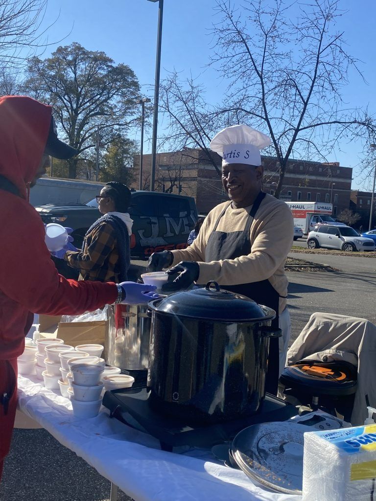 Vendor serving hot food from a large pot at an outdoor market table