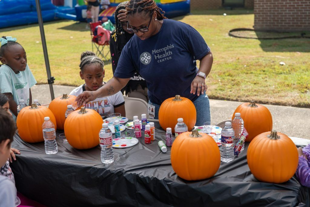 People decorating pumpkins at an outdoor table with paints and craft supplies