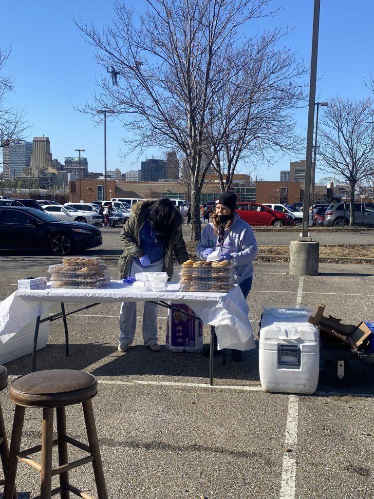 Outdoor food table with trays and supplies in a parking lot near a leafless tree