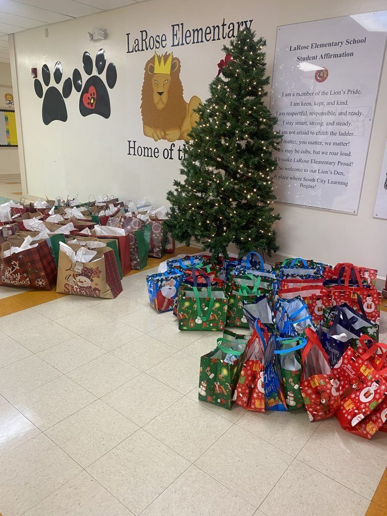 Holiday gift donations piled beside a decorated Christmas tree in a school hallway