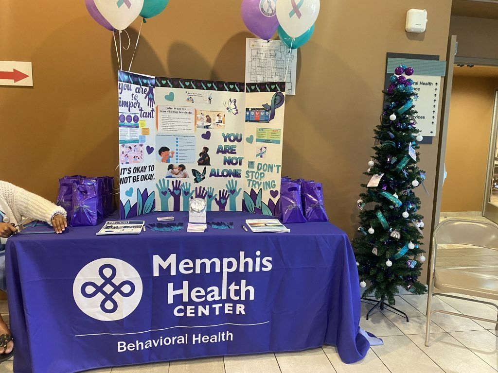 Memphis Health Center booth with purple tablecloth, balloons, posters, and a small decorated Christmas tree
