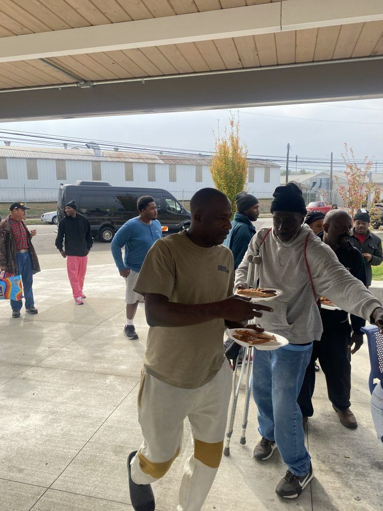 People walking under a covered outdoor area, one carrying a tray, with others in the background.