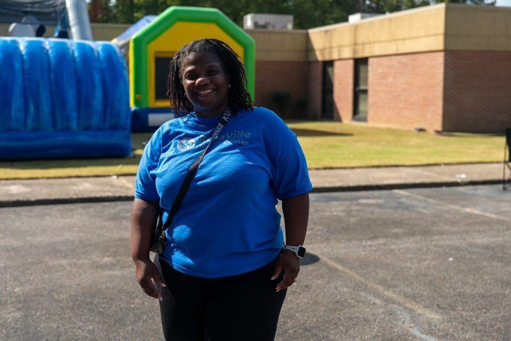 Woman in a blue shirt standing outdoors near a colorful inflatable structure.