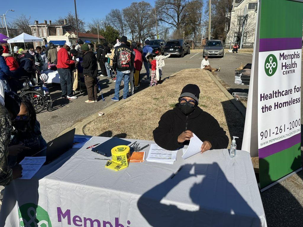 Outreach table at a community event with a masked volunteer and Memphis Health Center sign