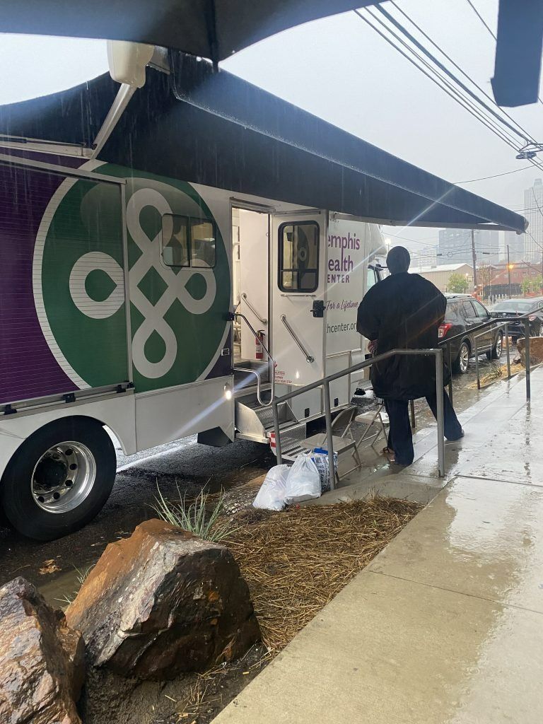 Food truck with black awning in a snowy outdoor market, with a person standing nearby.