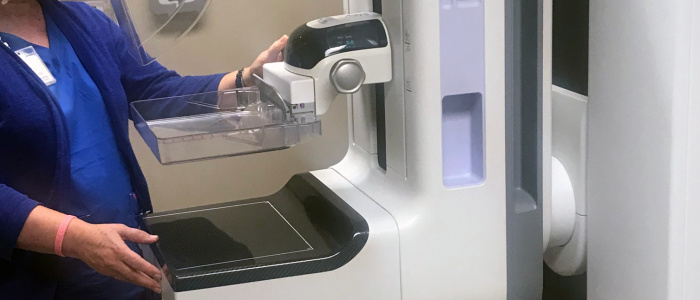 Person using a machine built into a white cabinet, holding a clear bin on a countertop