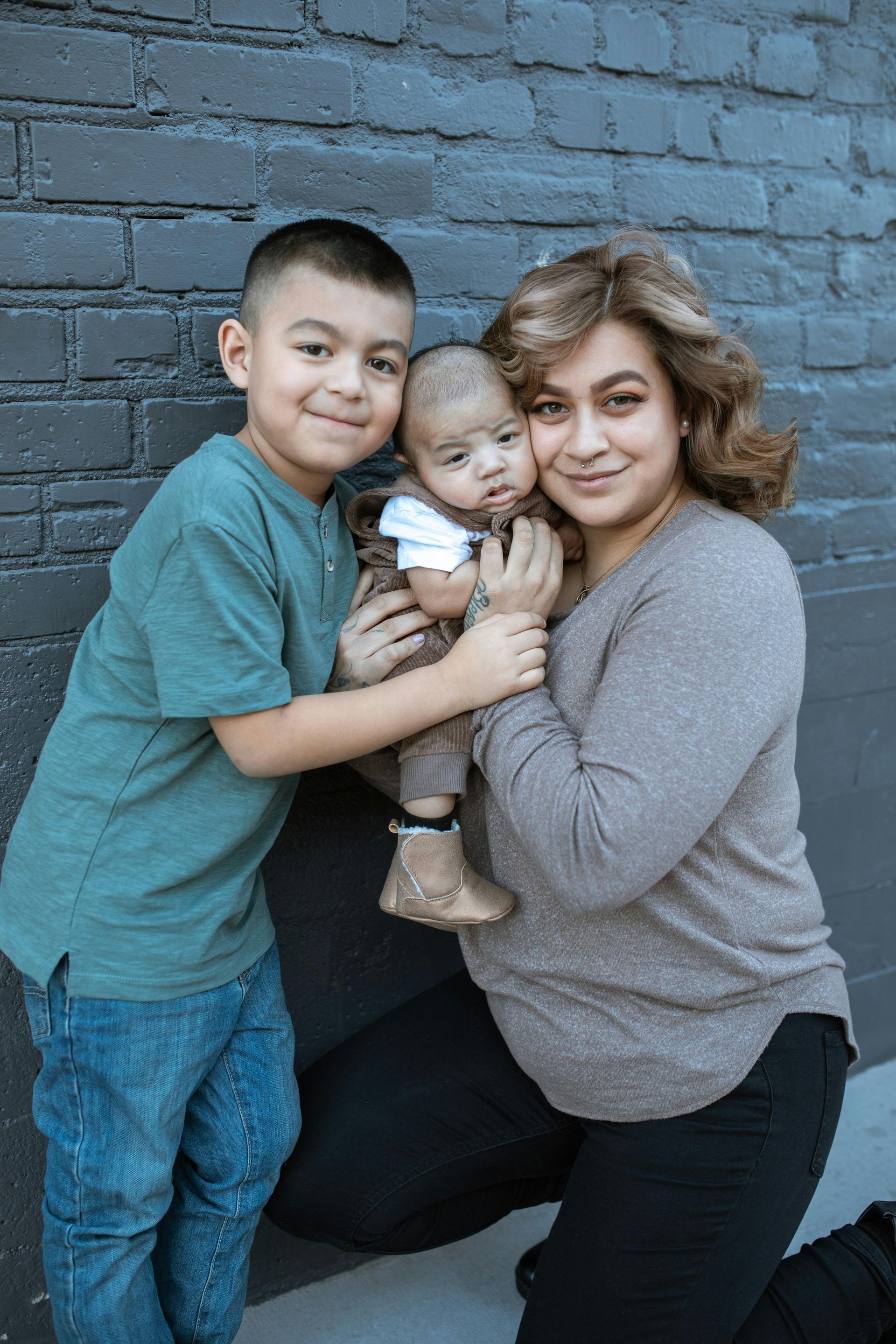 Three people hugging in front of a blue brick wall, smiling at the camera.
